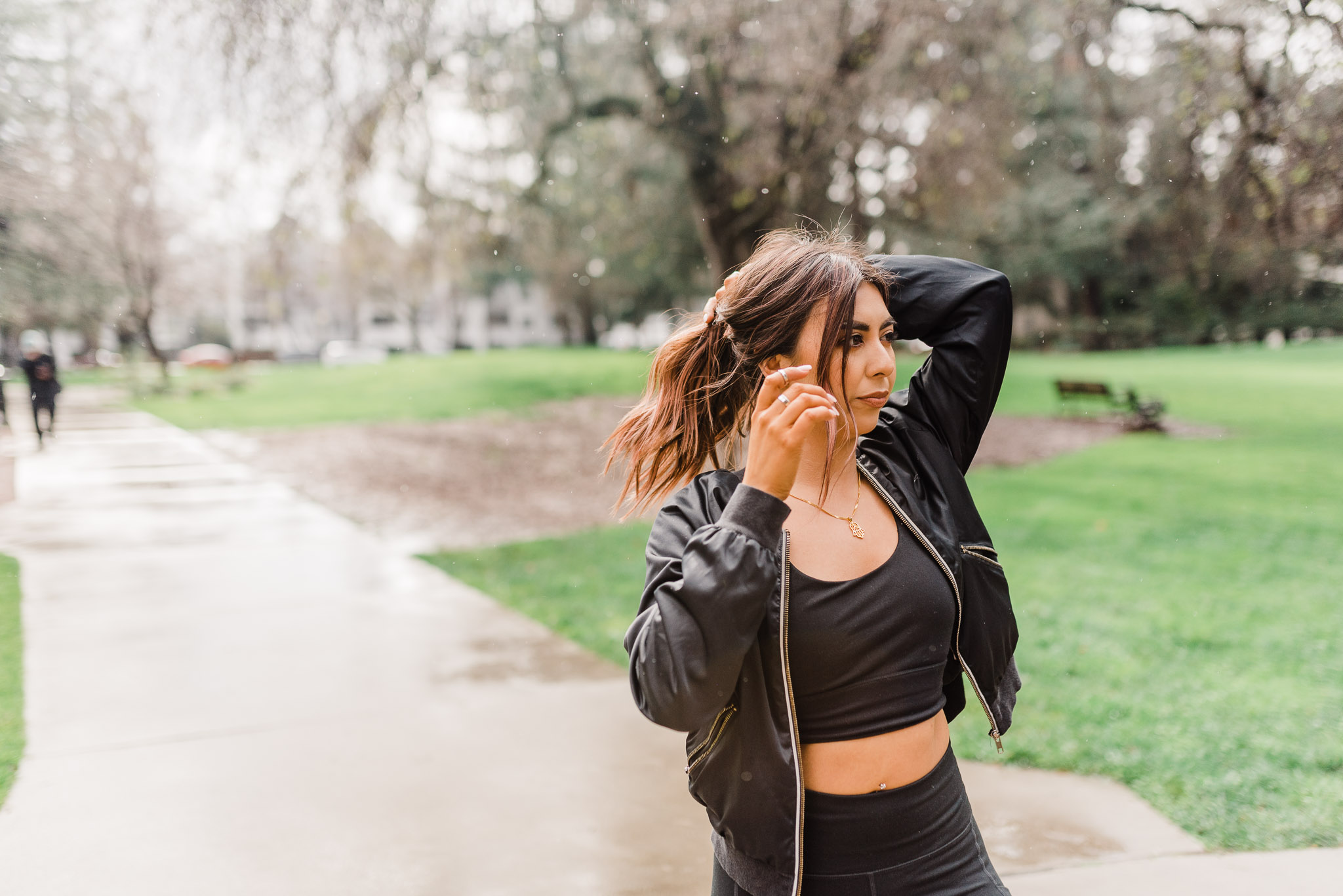 Fitness blogger wearing sports bra, legging, and windbreaker style jacket. Putting her hair in a ponytail.