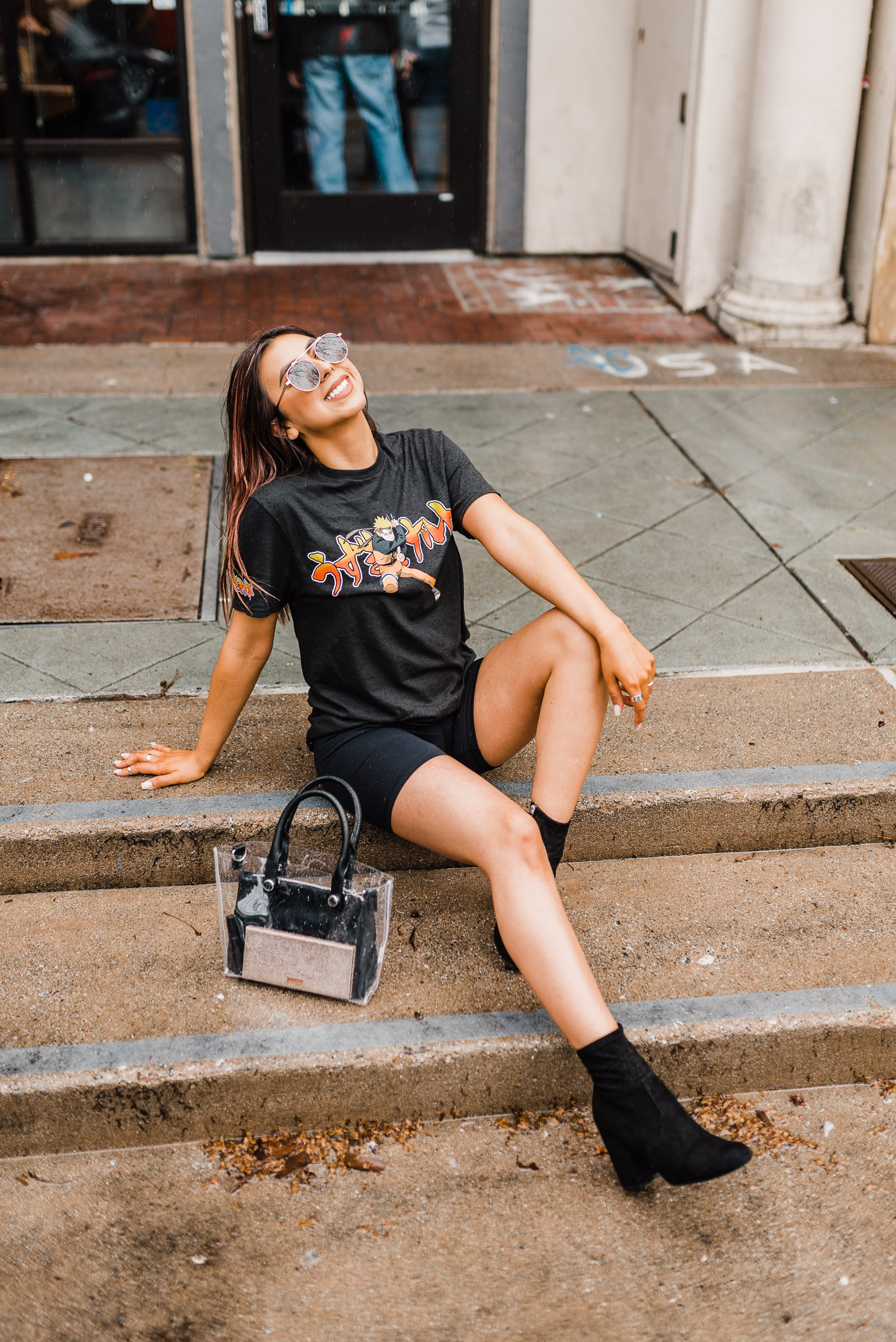 Fashion blogger wearing sunglasses and a Naruto shirt. Sitting on the sidewalk.