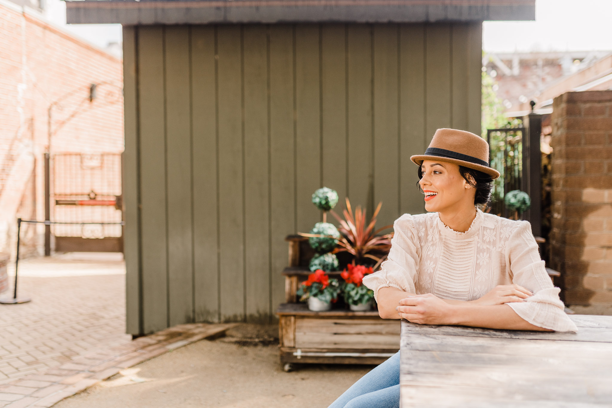Woman wearing a hat sitting on a picnic bench outside. She's looking away from the camera.