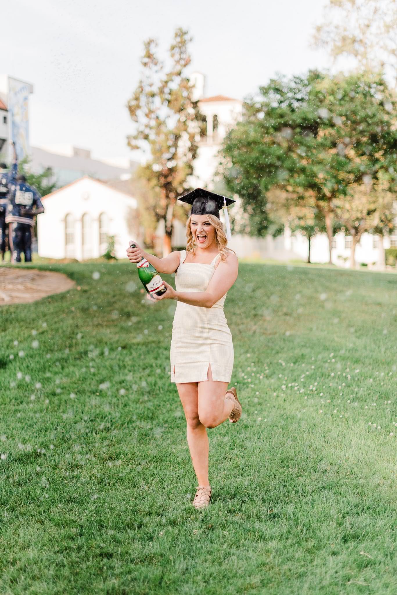 College grad popping champagne wearing white dress