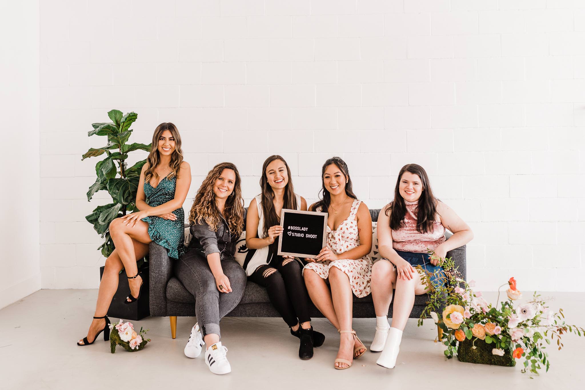 Group shot of everyone sitting on the couch holding a sign that says "#BossLady Studio Shoot."