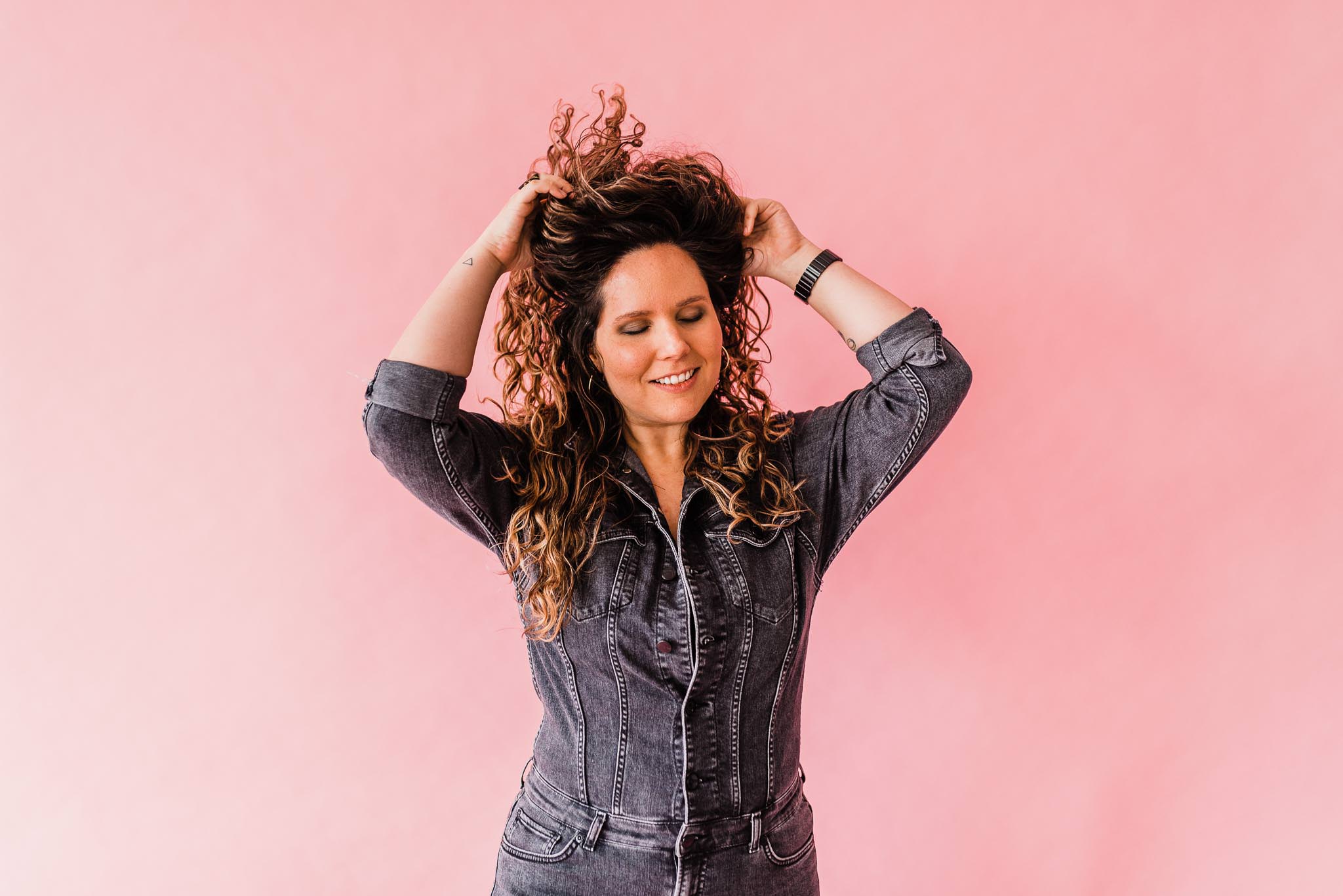 Woman doing a hair flip in front of a pink seamless paper backdrop.