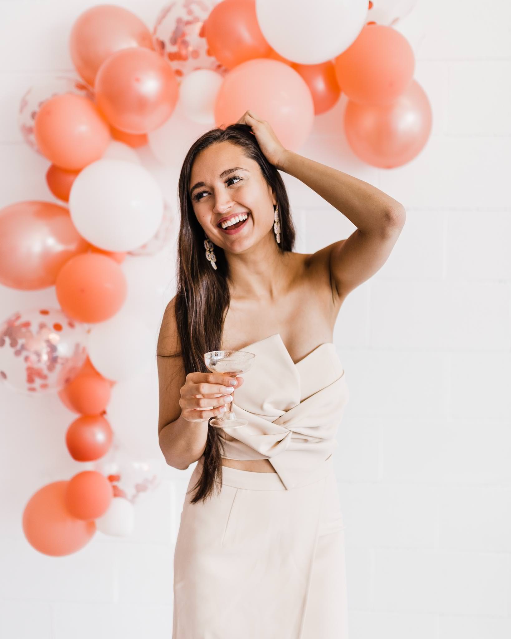Lifestyle shot of a blogger laughing and holding rose in front of a pink and white balloon garland.