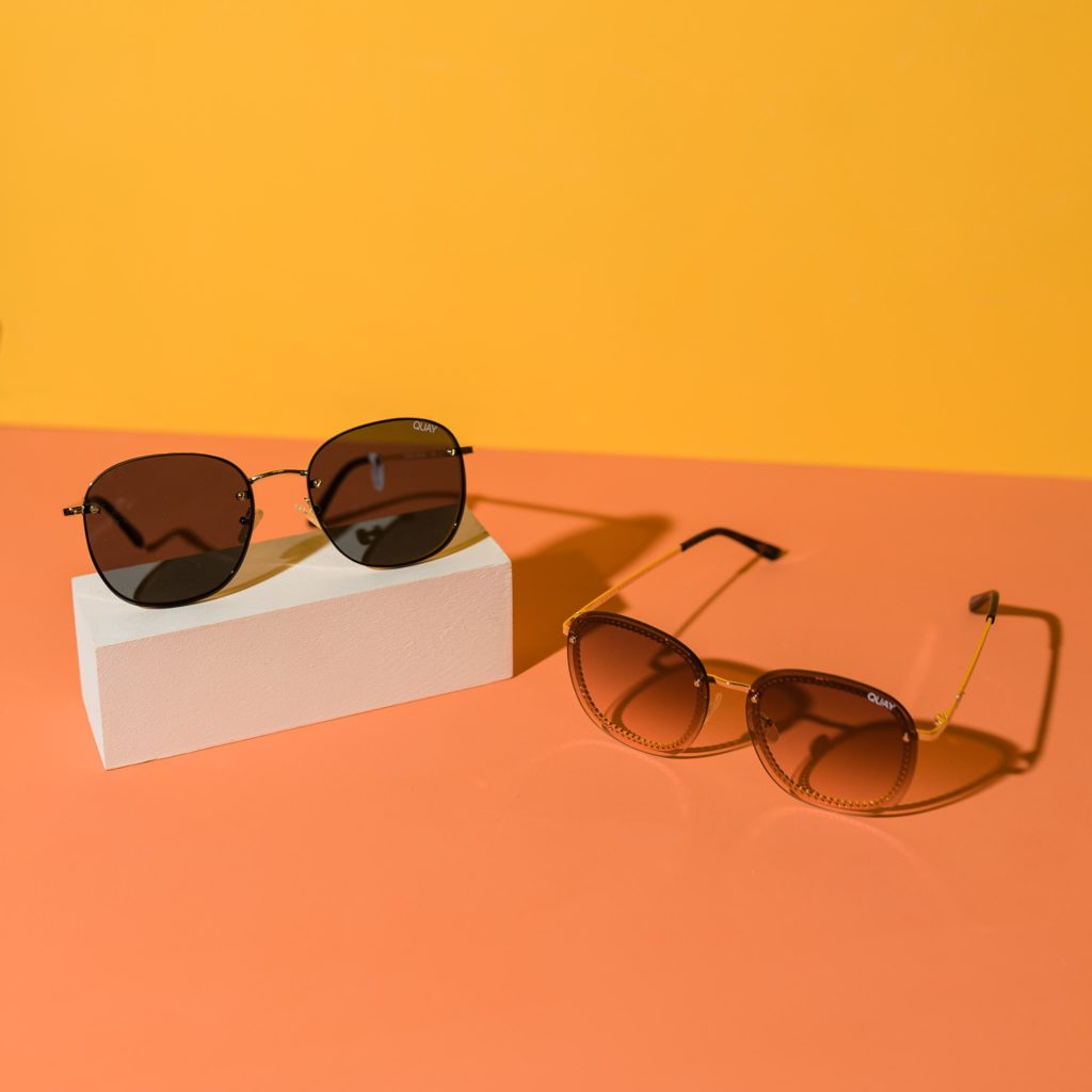 2 pairs of Quay sunglasses on an orange and yellow background.