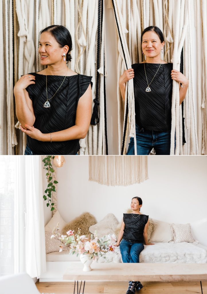 A woman wearing a black shirt against a macrame wall. She's wearing her own custom made jewelry.