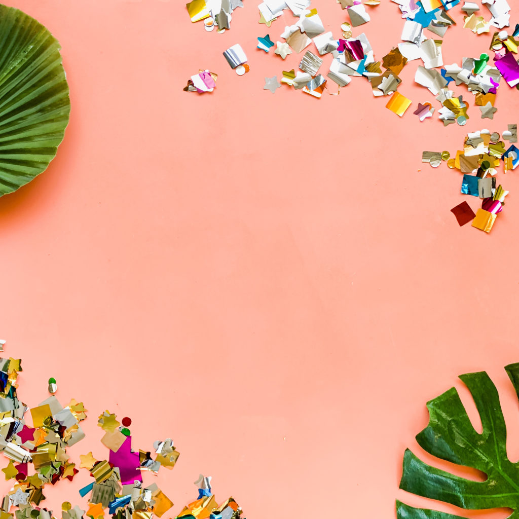 pink flat lay with confetti and tropical leaves