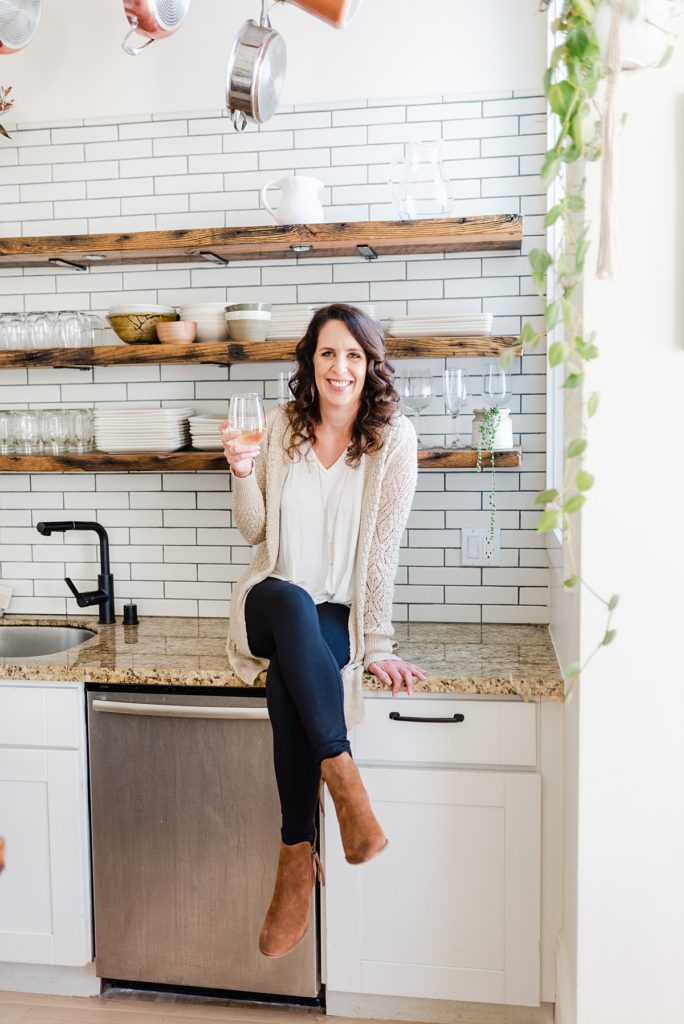 branding photo of woman sitting on a kitchen counter holding a glass of wine.