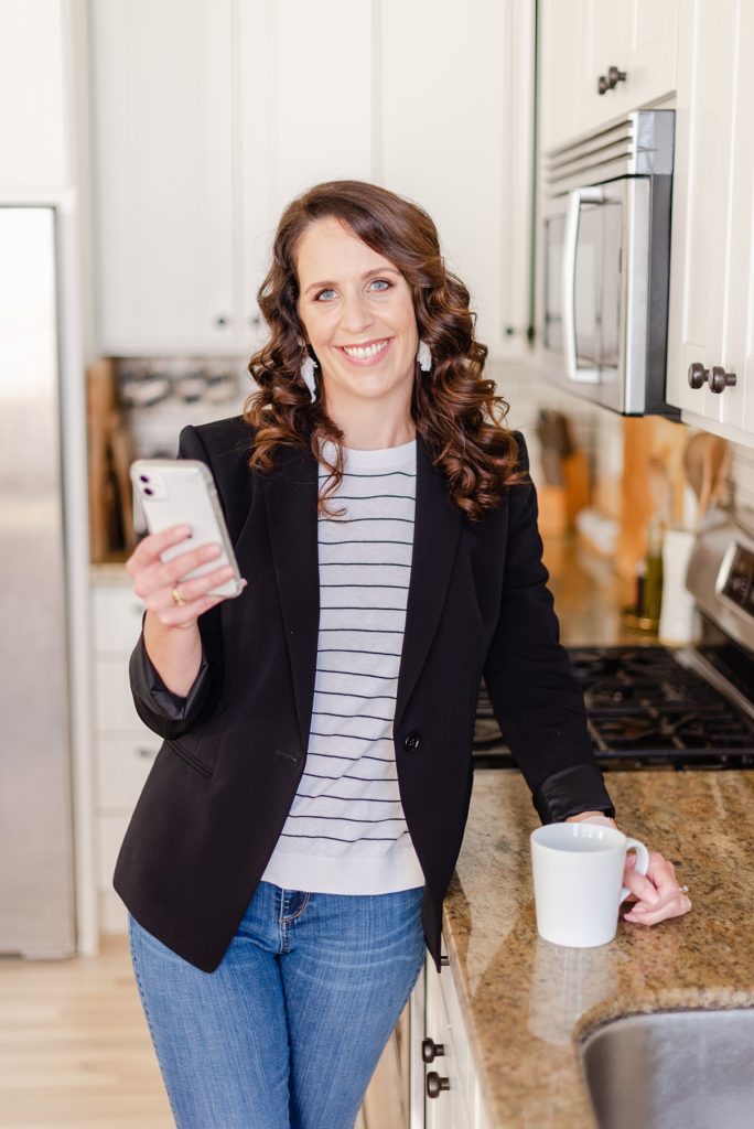 branding photo of a woman leaning against a kitchen counter. she's on her phone and holding a mug.