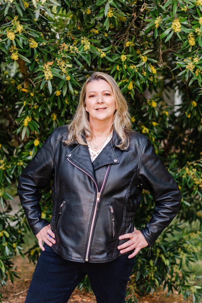 Woman with her hand on her hips. She's wearing a black leather moto jacket.