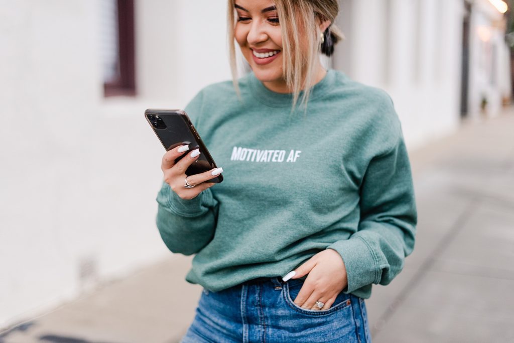 woman wearing "motivated AF" sweatshirt on her phone