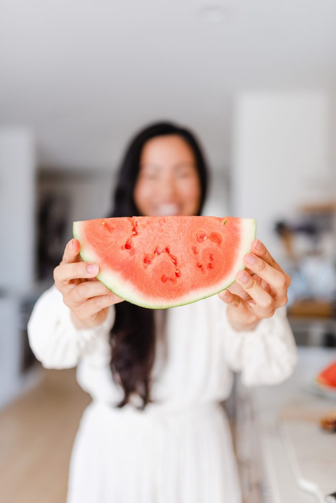 Woman in white long-sleeved dress is holding out a watermelon