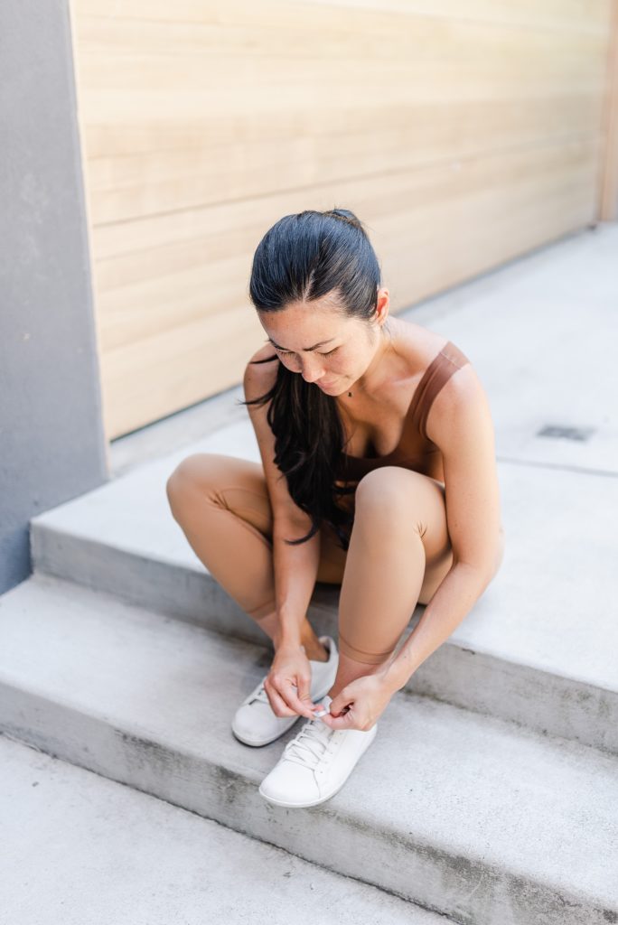 Woman in brown sitting down on a step while tying her shoe