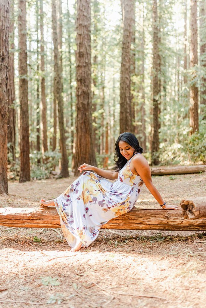 woman in a dress sitting on a fallen tree trunk on the forest