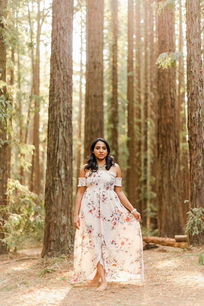 woman standing amongst the trees while holding her dress