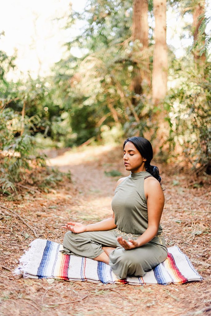 a meditating woman sitting on a blanket on the forest floor