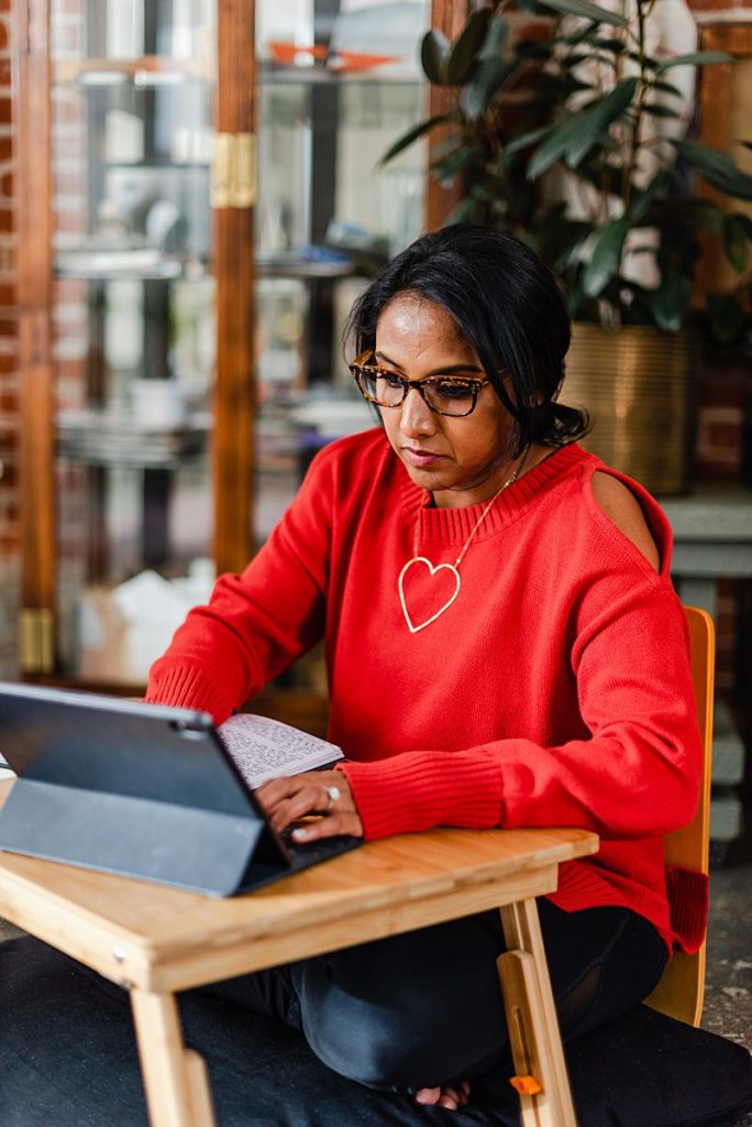 woman wearing a red long-sleeved blouse is typing on her laptop