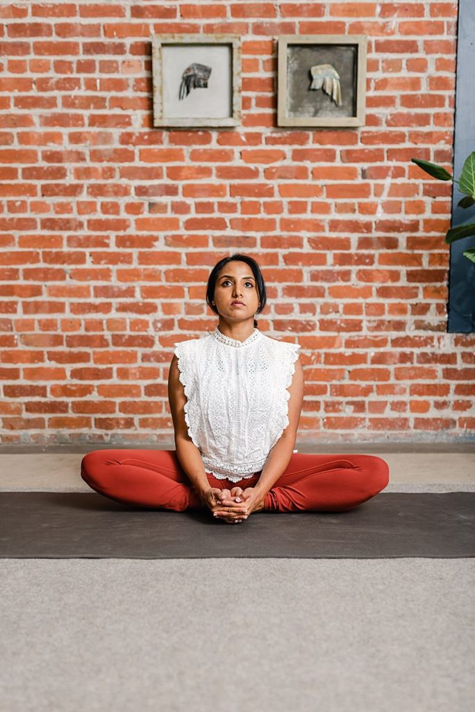 a woman is sitting on a yoga mat while she's holding the soles of her feet together