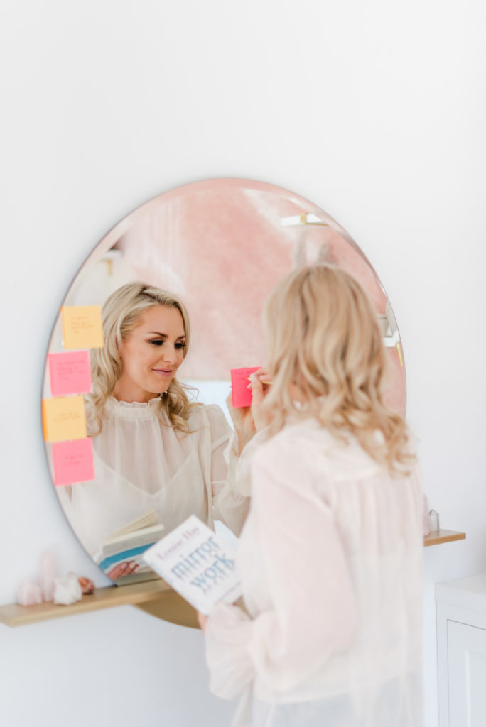 woman in white looking at her reflection in a round mirror