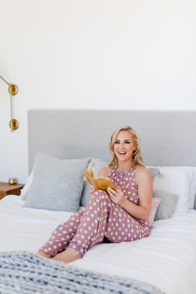 woman lounging in her bed while holding a book