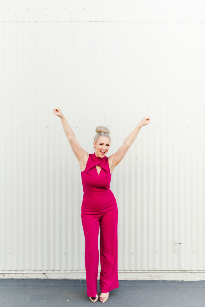 woman in pink raising both her arms and smiling