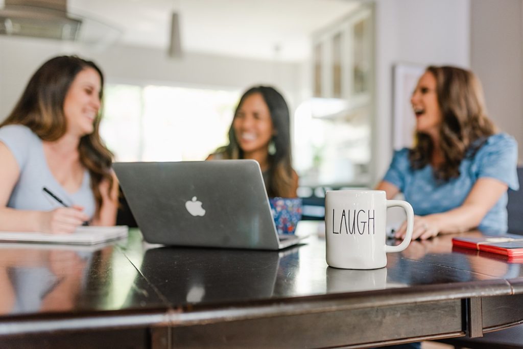 a laptop and a mug on top of a table. the mug has the word 'LAUGH' on it with three women laughing in the background