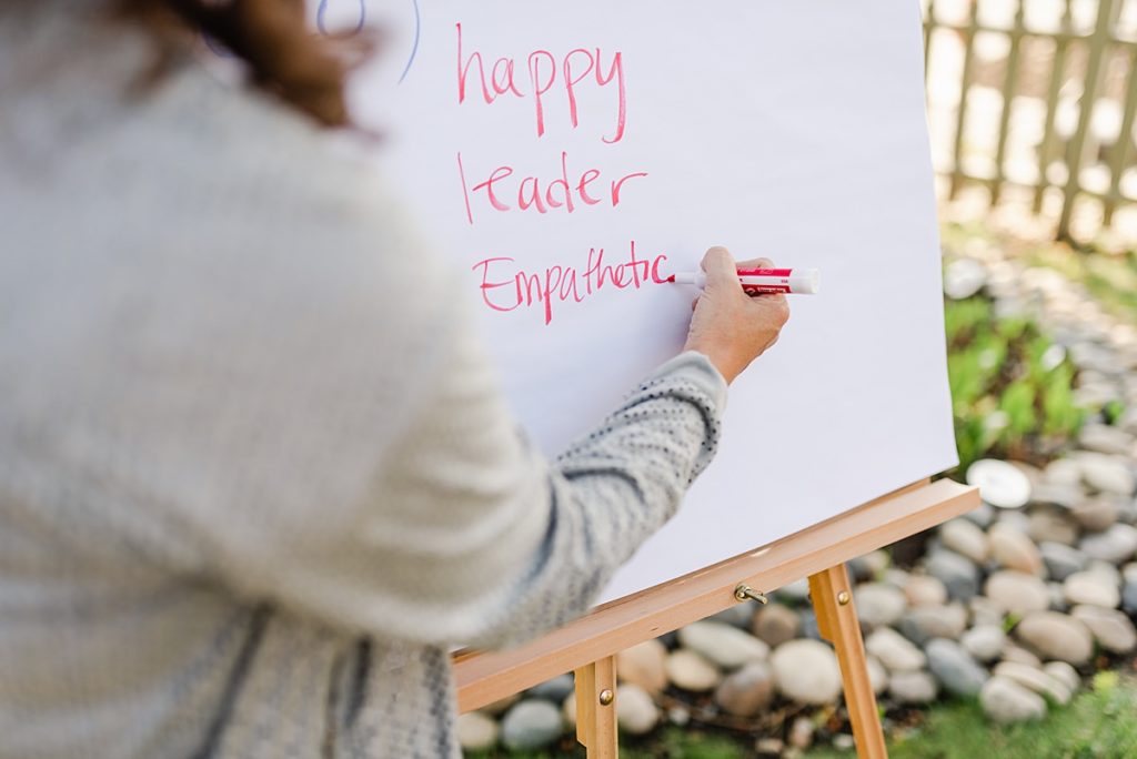 woman writing words on a board. the words are: happy, leader, empathetic