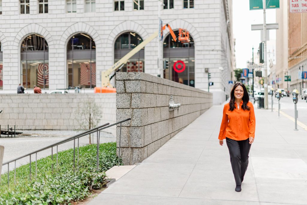 woman in orange blouse is smiling while walking downtown
