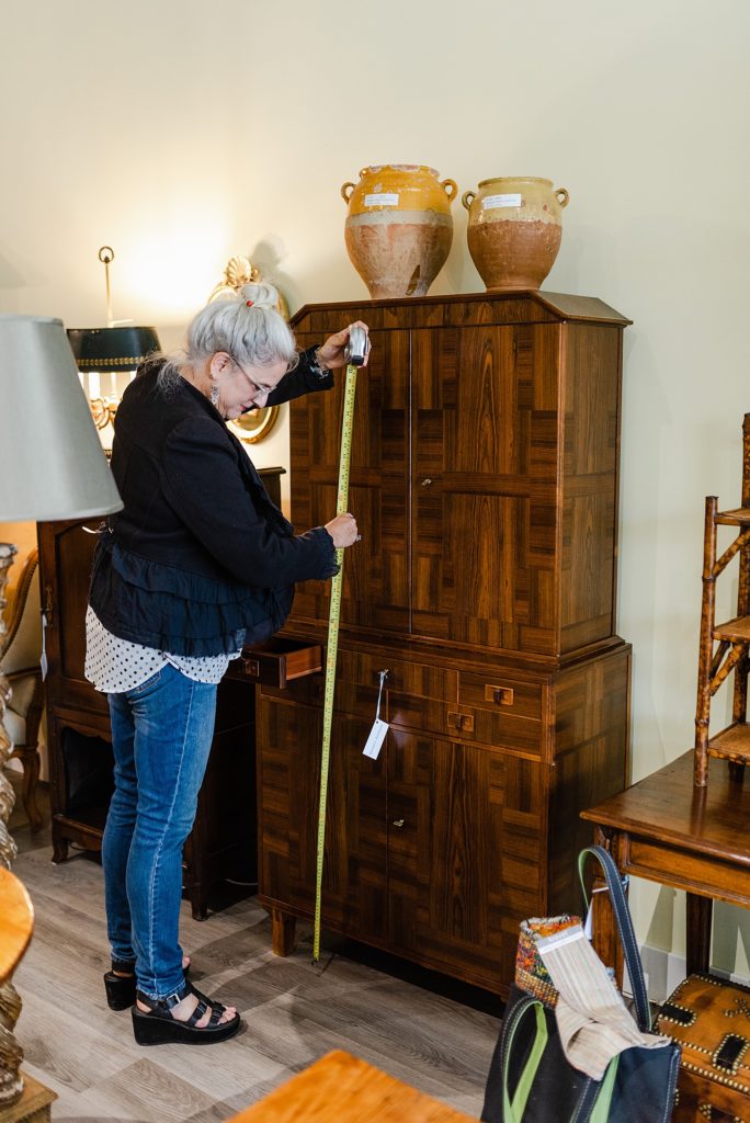 woman measuring from the floor to the top of a cabinet using a metre tape. there are two brown vase son top of the cabinet