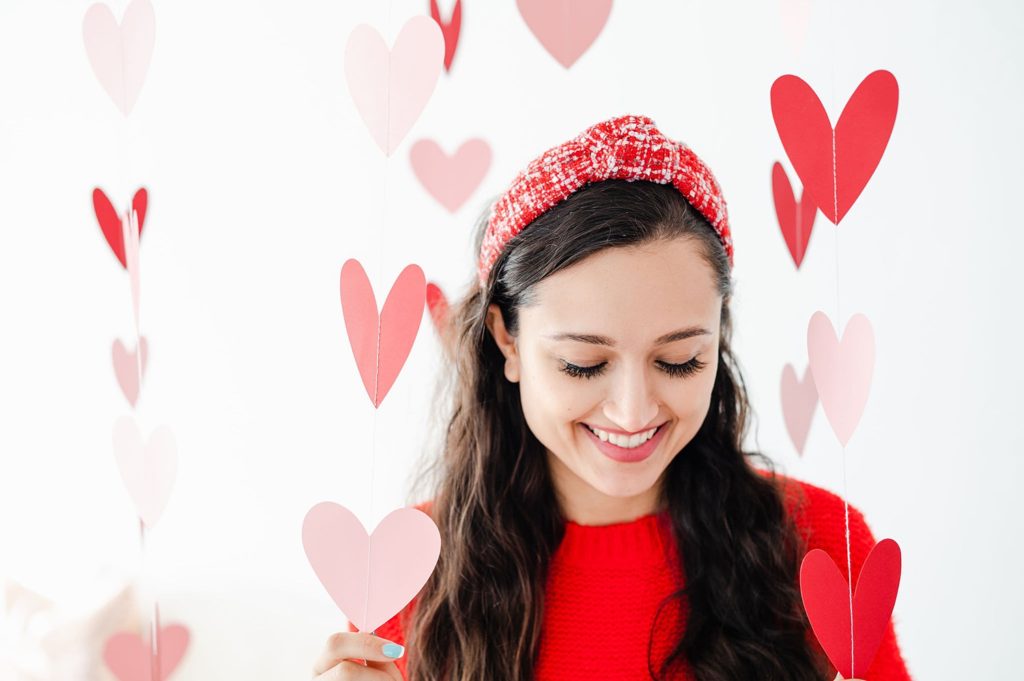 red shimmer tweed headband on a model. the model is in a bright red sweater and there are hearts hanging from the ceiling