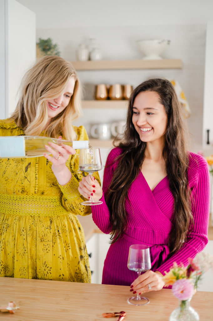 Woman pouring a glass of wine for another woman at kitchen island. 