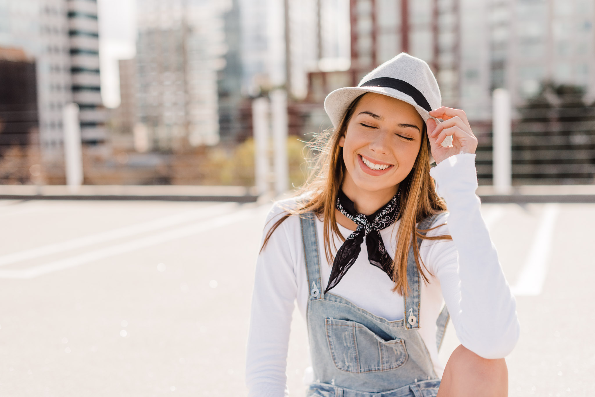Teen sitting on rooftop with cityscape in the background holding her hat, by Emily Kim Photography.