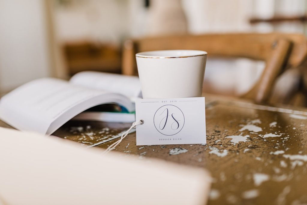 A business card with a "JS" emblem leaning up against a coffee cup.