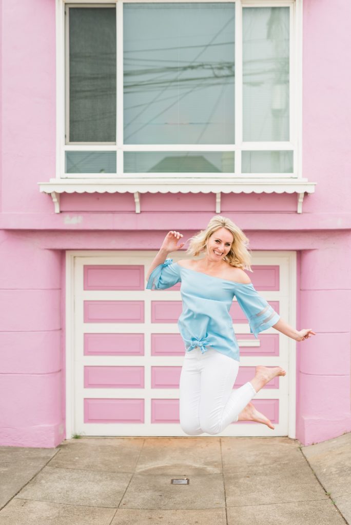 woman jumping in front of a pink house in San Francisco