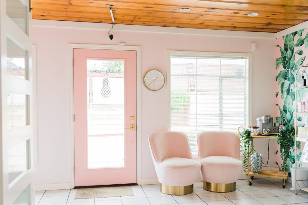 A pink, tropical salon. There are two plush pink chairs and a tropical print wall. Hair salon branding photos.