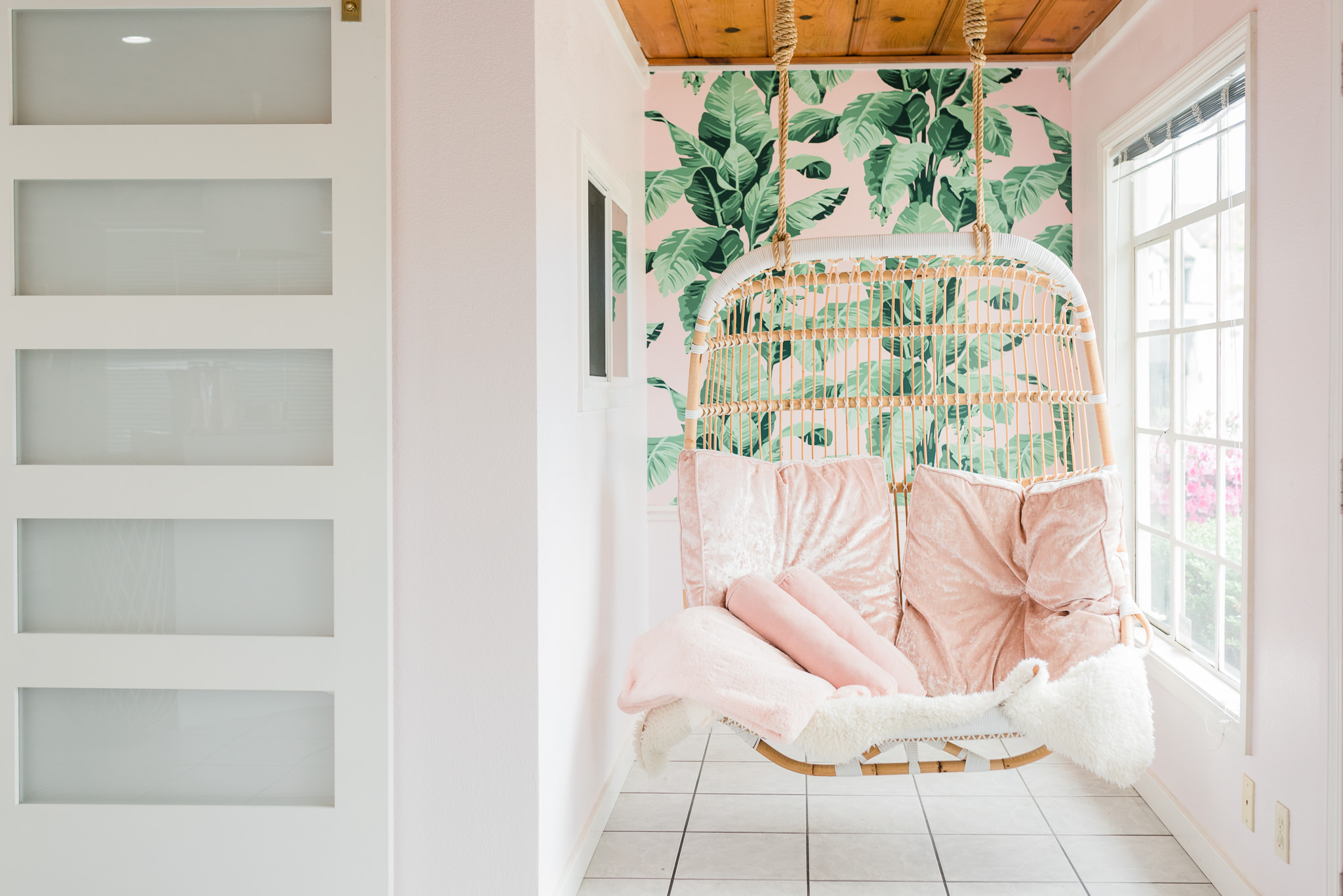 hanging chair with peach cushions. there's a leaf mural on the wall behind the chair.