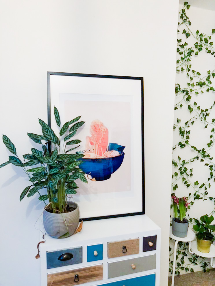 a dresser with a calathea plant and a painting sitting on top.