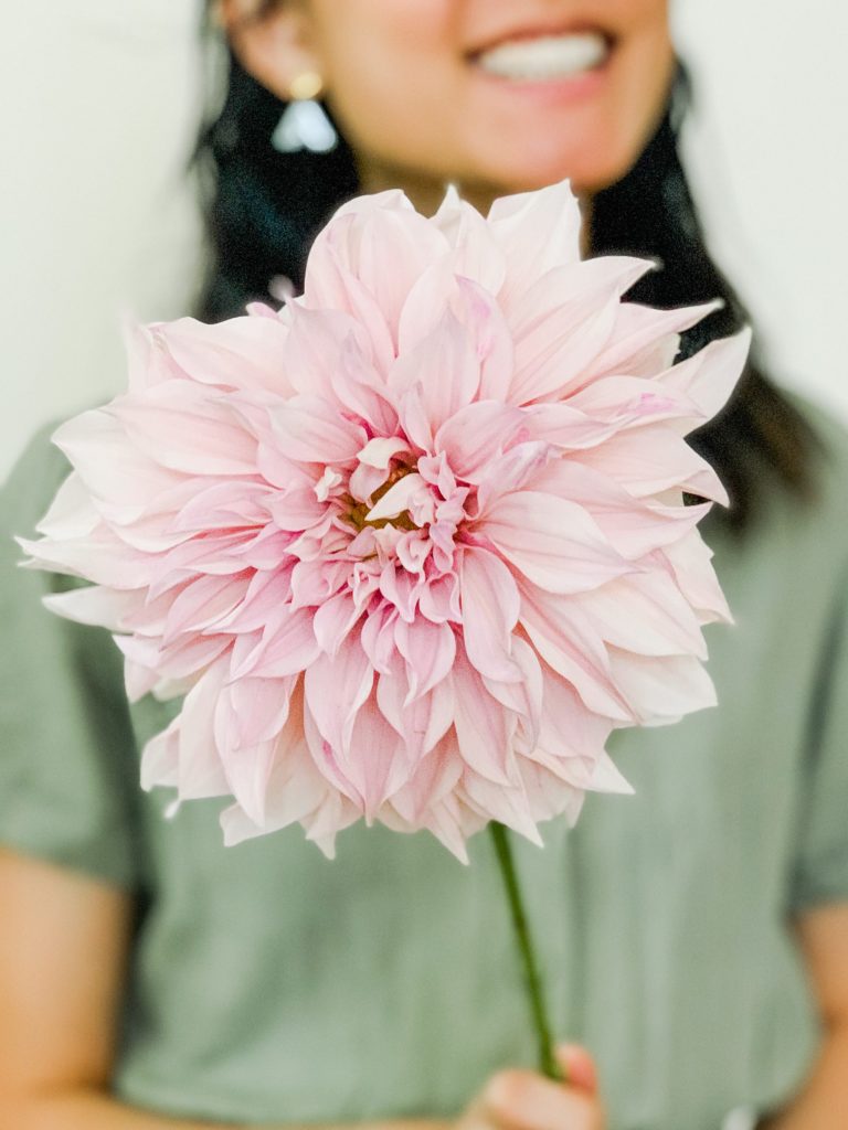 Woman wearing a green jumpsuit, sitting on the floor holding a pink dahlia.