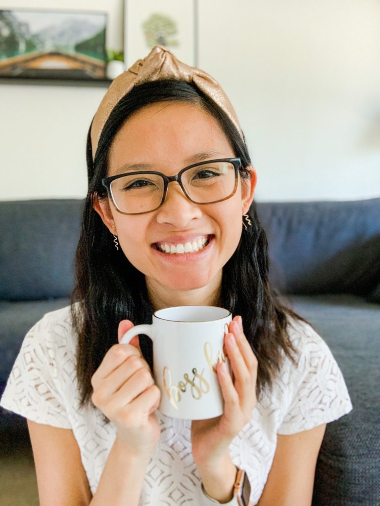 Woman wearing a white shirt and gold headband sitting on the floor holding a boss lady mug.