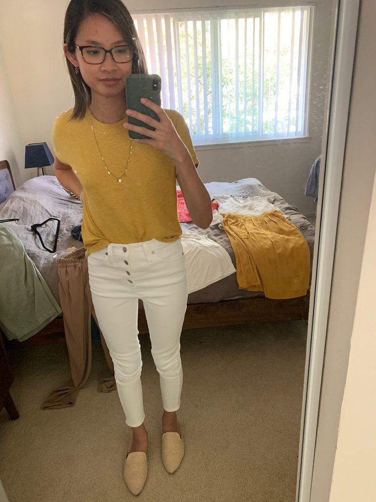 mirror selfie of a woman wearing a yellow t-shirt, long necklace, and white denim.