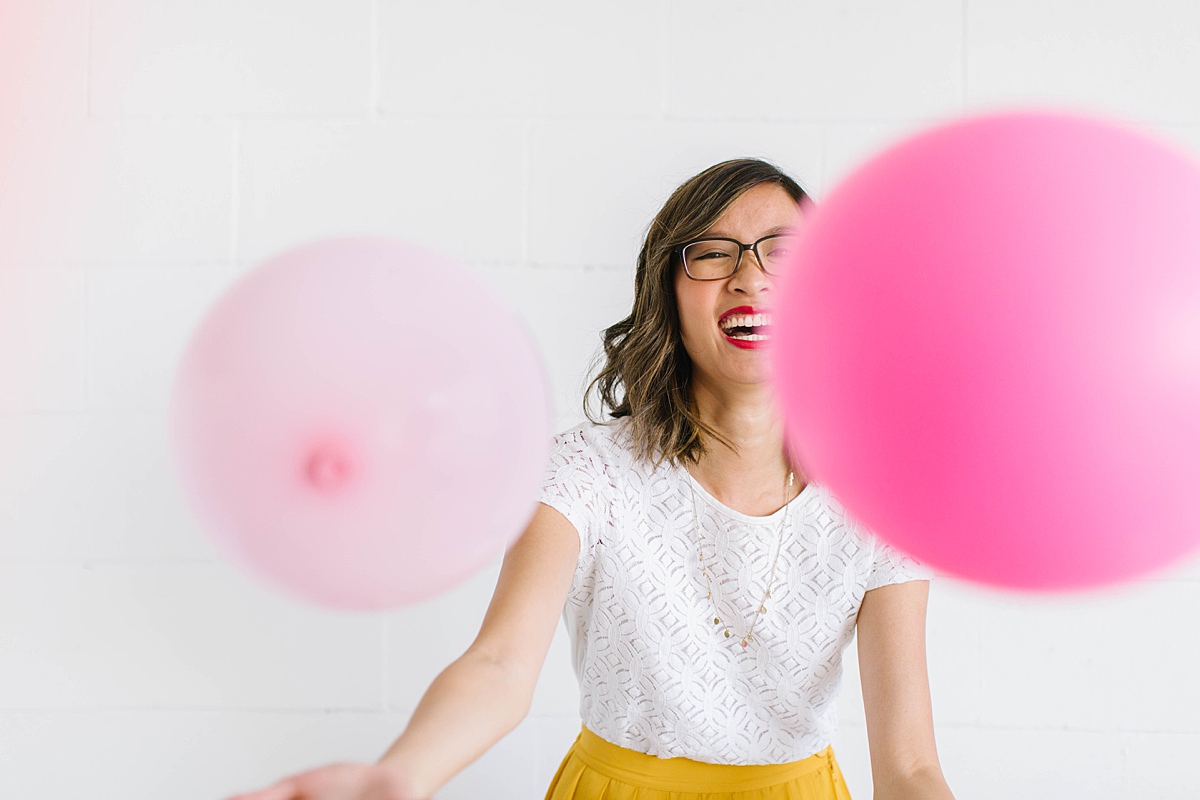 woman wearing a white shirt smiling, there are pink balloons flying around.