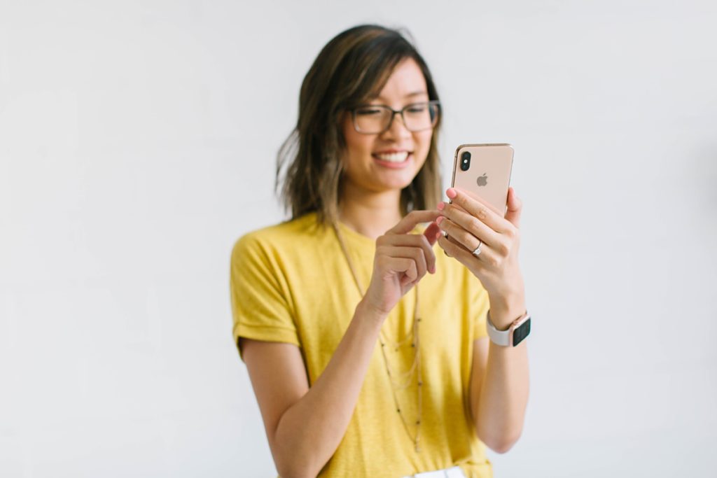 Asian woman wearing a yellow t-shirt using her iPhone.