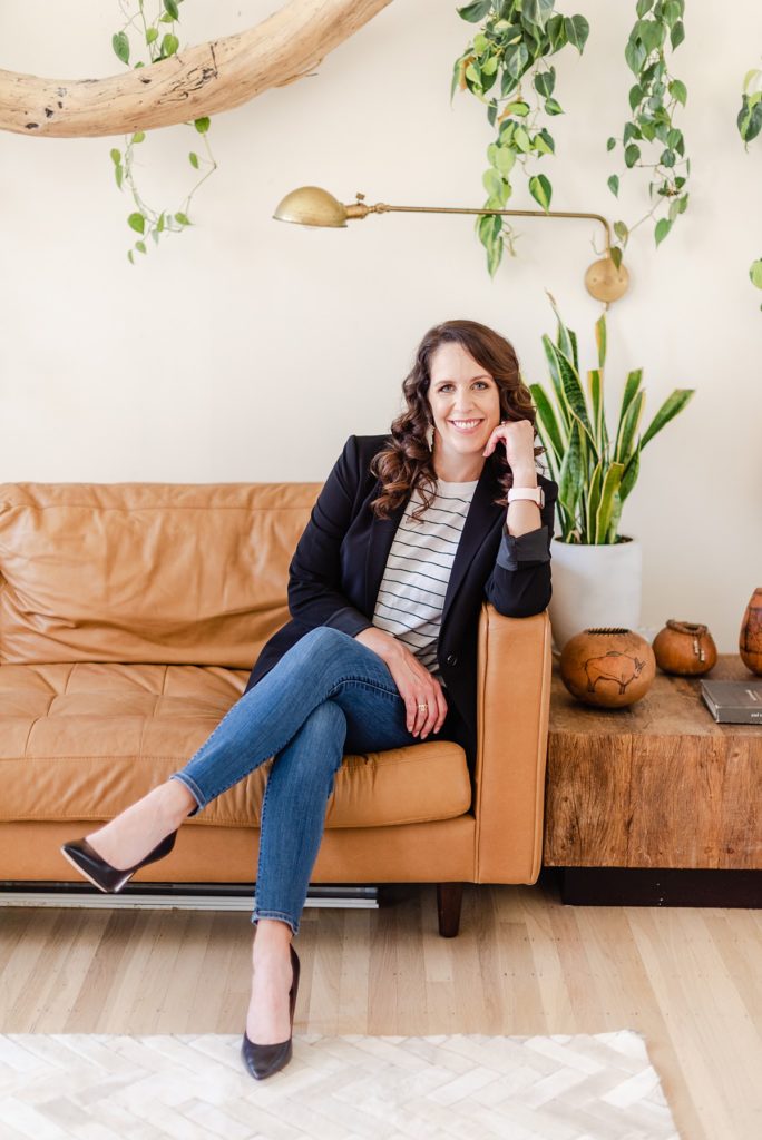 headshot of interior designer sitting on a light brown leather couch.