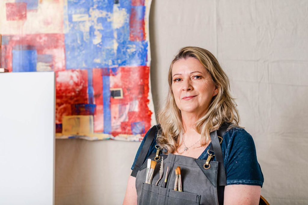 Portrait of an artist in her studio. She's wearing an apron with paint brushes.