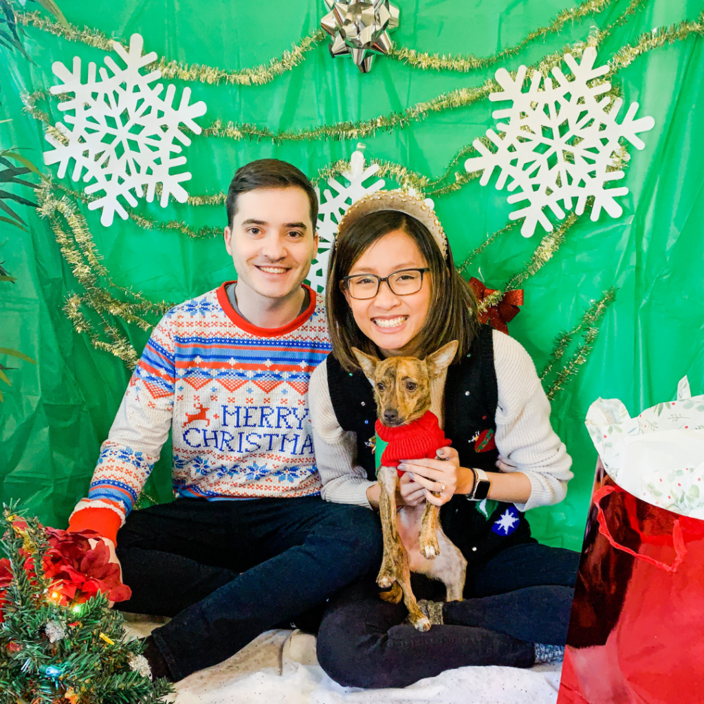 couple and their dog decked out in holiday attire in front of a green backdrop