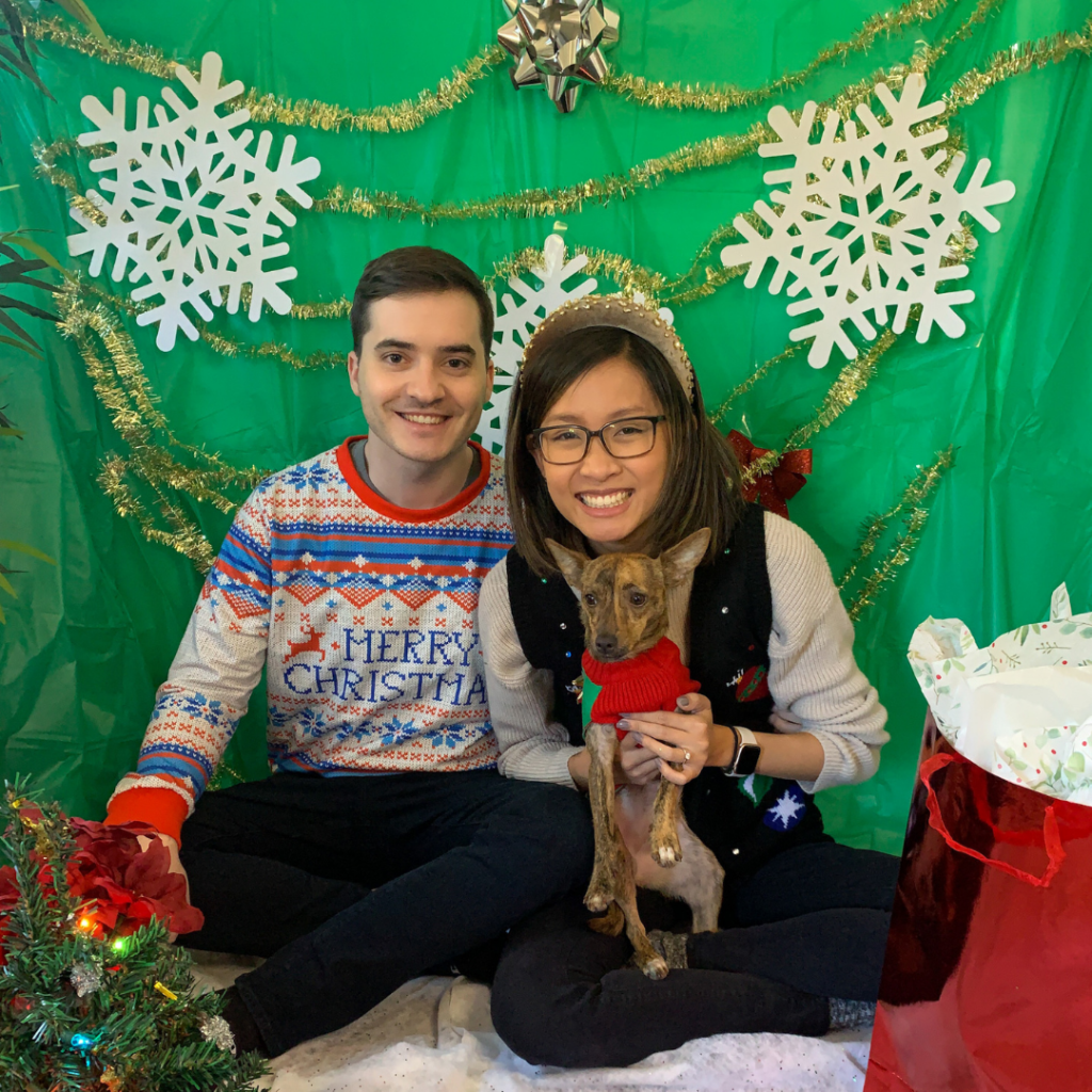 couple and their dog decked out in holiday attire in front of a green backdrop