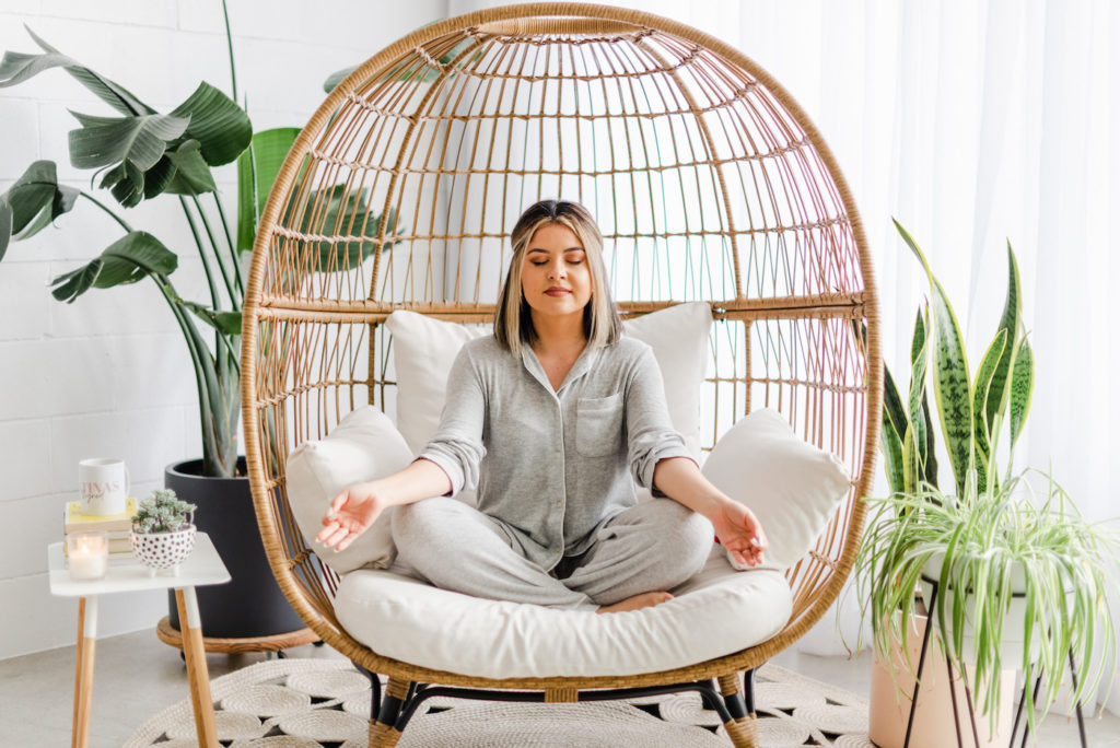 Woman in pajamas meditating in an egg chair