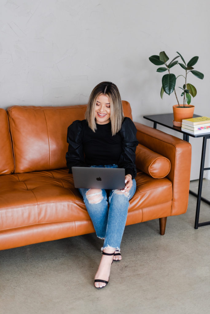 woman sitting on a leather couch using her laptop