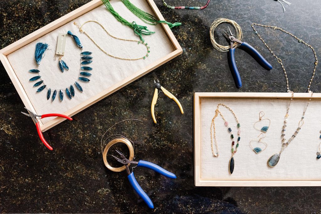 Two trays, three pliers, and rolls of strings on top of a dark surface. There are two necklaces and a pair of earrings on each of the trays.
