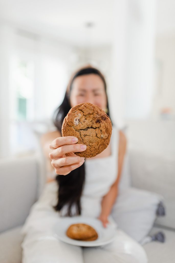 Woman in white holding out a cookie and partially covering her face