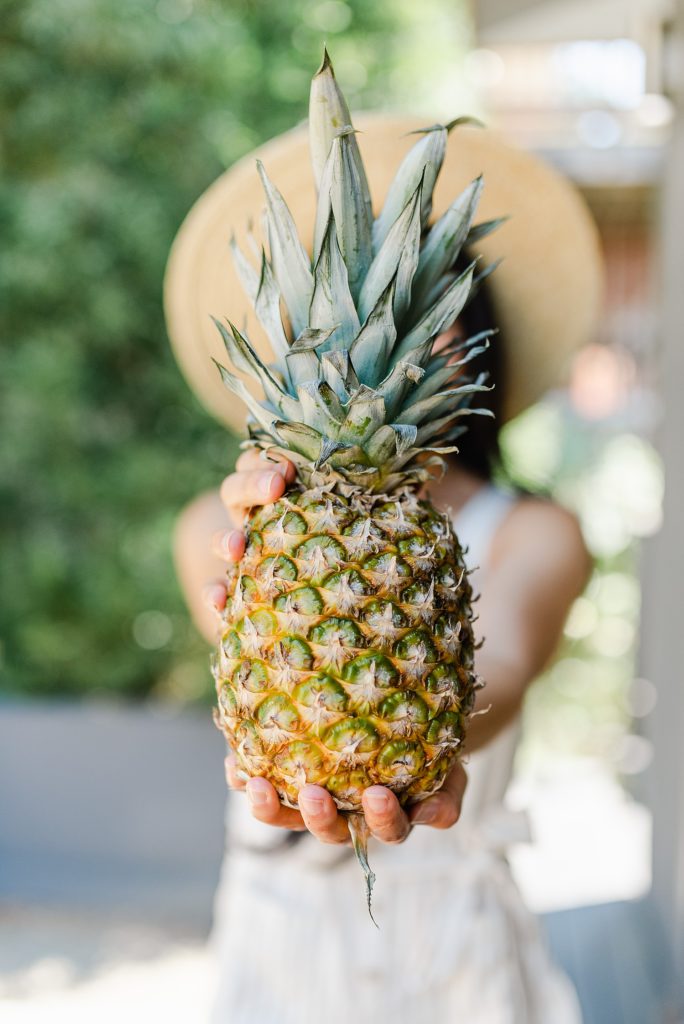 Woman holding a pineapple in front of her covering her face.